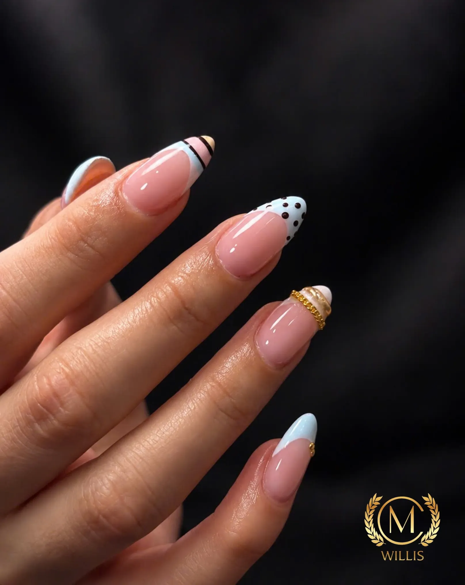 Natural almond nails with baby blue French tips, black polka dots, stripes and a gold chain charm