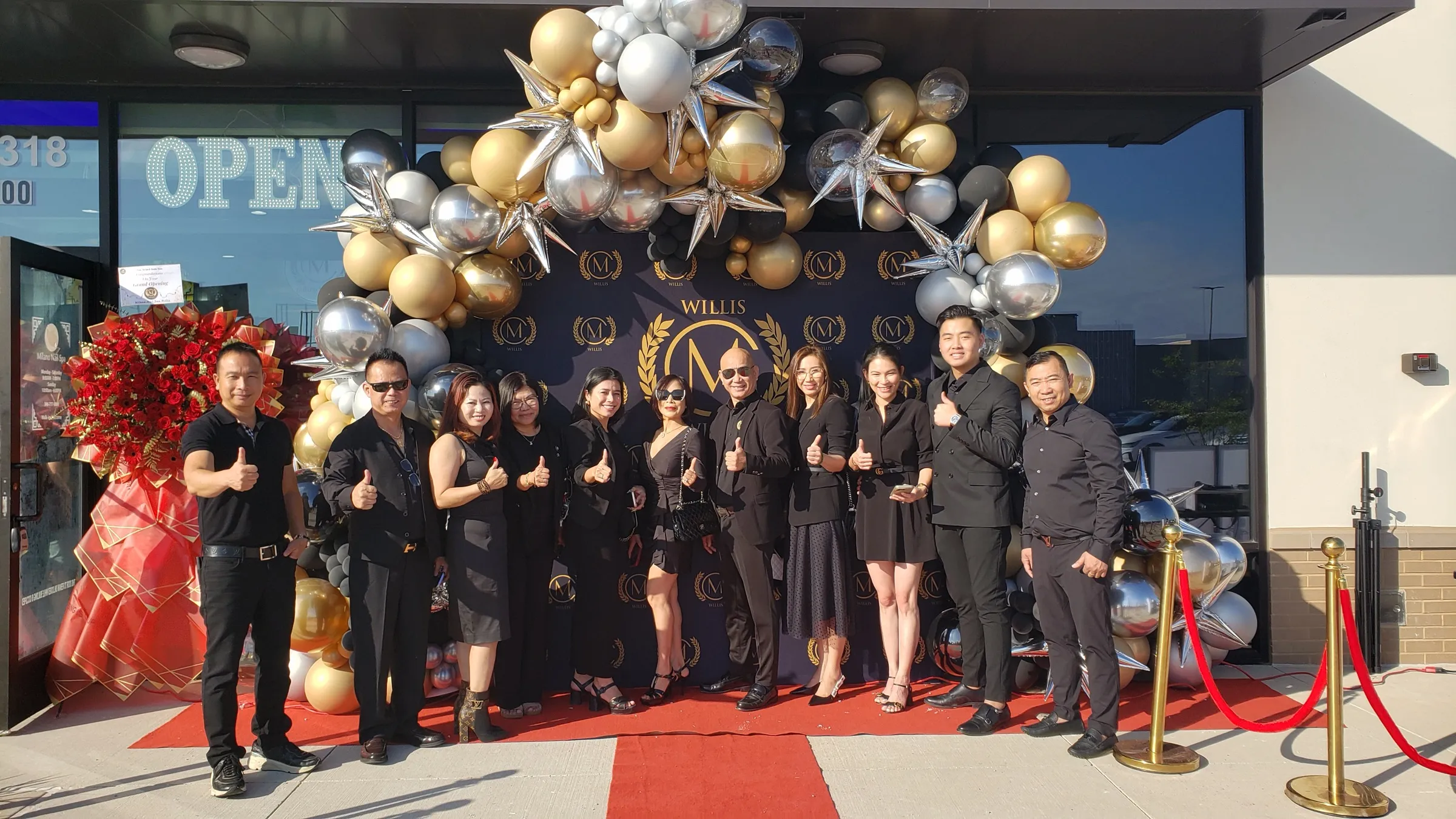 The Milano Nail Spa Willis team giving thumbs up in front of the gold balloon arch on grand opening day