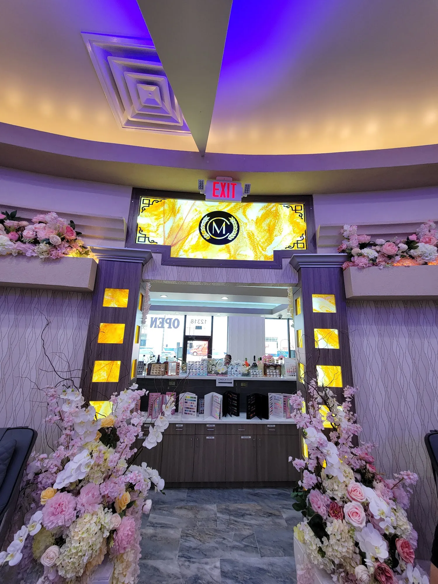 Milano Nail Spa reception with the gold M crest framed by pink and white floral arrangements